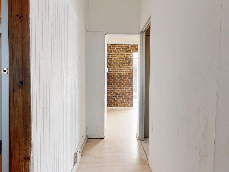 A vacant hallway featuring beadboard wall paneling, laminate flooring, and a view through to an exposed brick wall section.