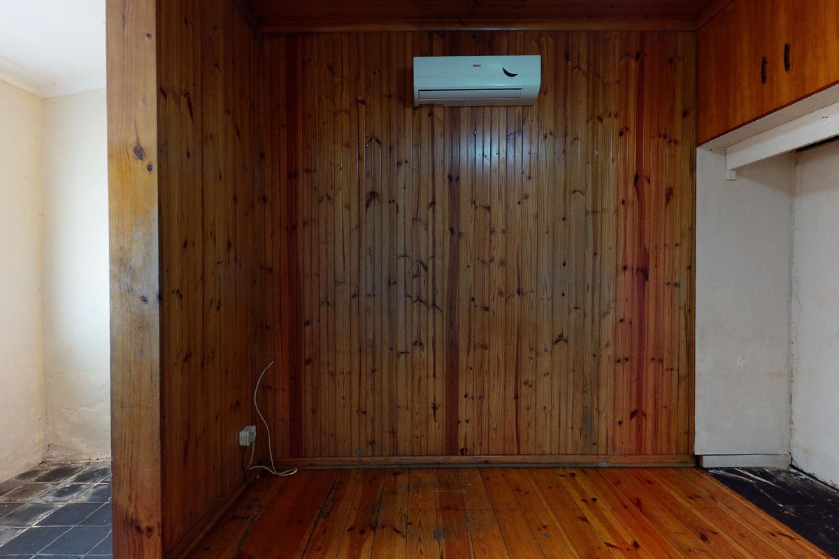 An empty living area featuring timber wall paneling, polished timber flooring, and a wall-mounted split-system air conditioning unit.