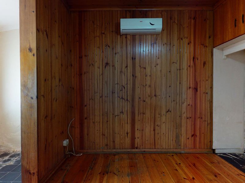 An empty living area featuring timber wall paneling, polished timber flooring, and a wall-mounted split-system air conditioning unit.
