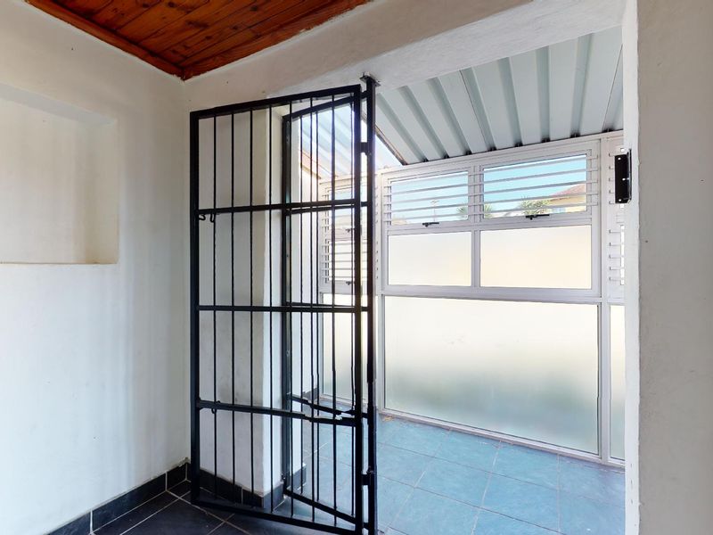A covered patio area featuring tiled flooring, a timber ceiling, and a secure metal gate, providing a functional outdoor transition space.