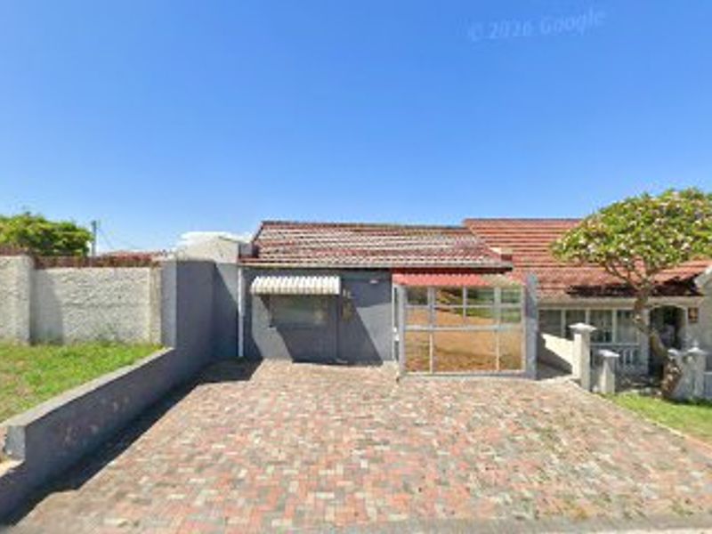 Front view of the property featuring a paved driveway, boundary wall, and tiled roof structure.