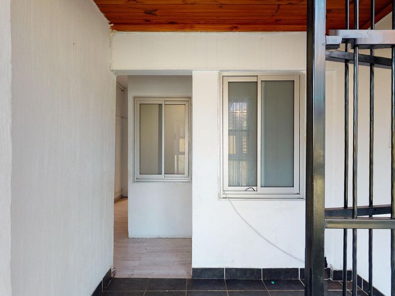 A covered patio area featuring tiled flooring, timber ceiling, and aluminium sliding windows, secured by a metal gate.