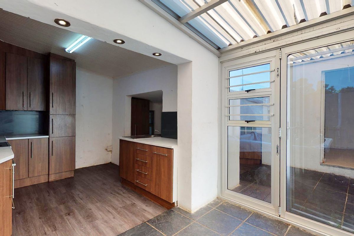 A functional kitchen area featuring wood-finish cabinetry, laminate countertops, and direct access to an outdoor space through a sliding glass door.