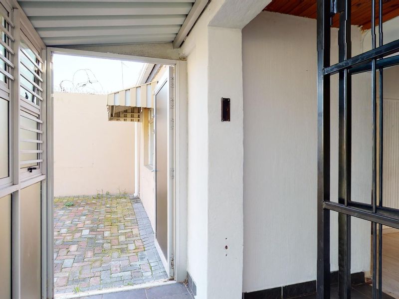 A covered patio area featuring a security gate, paved courtyard access, and an exterior awning, providing a functional transition space between indoor and outdoor areas.