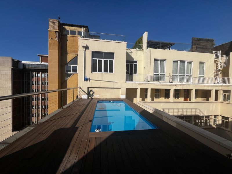 Elevated rooftop pool area featuring timber decking, stainless steel balustrades, and views of the surrounding apartment building architecture.