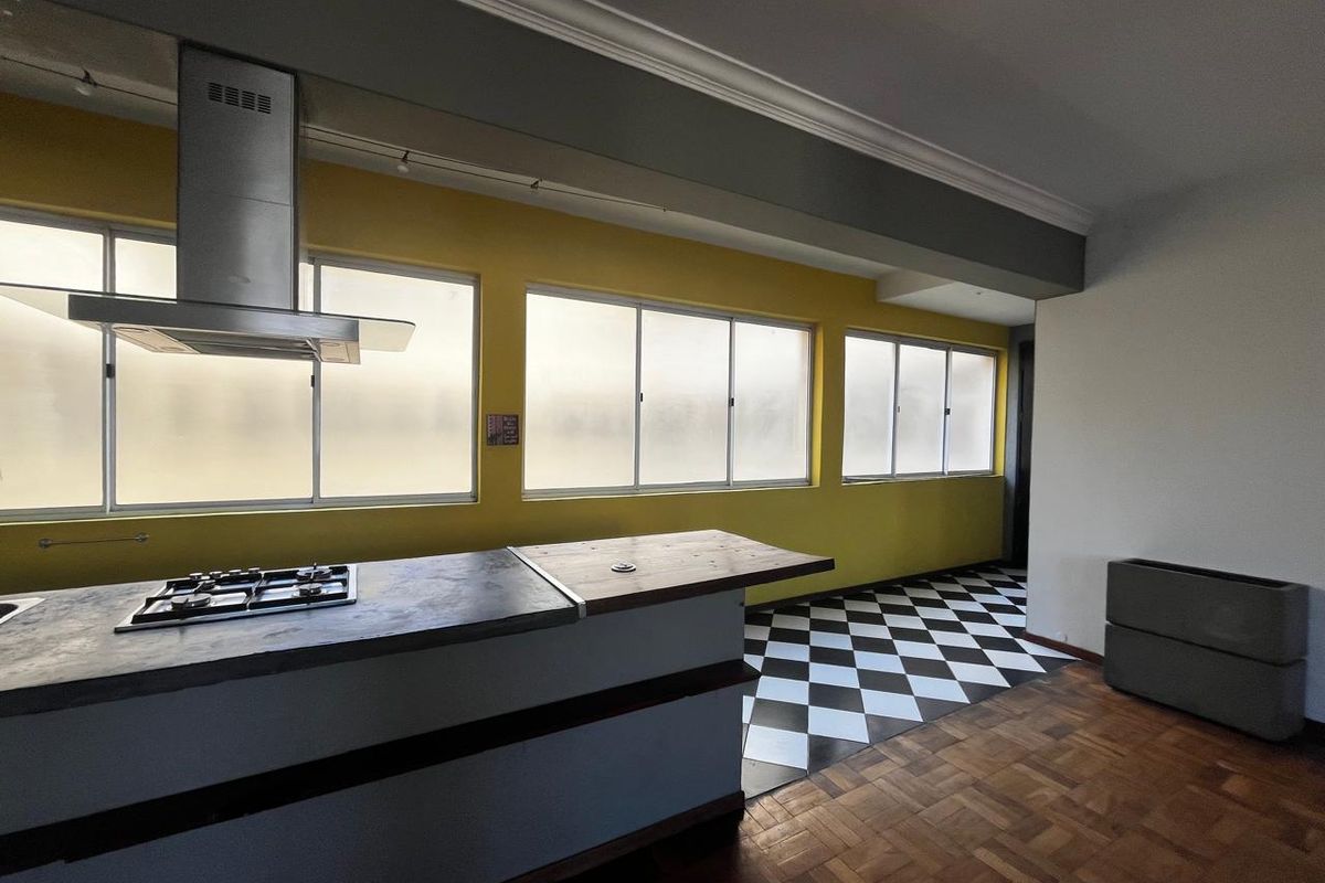 Spacious kitchen area featuring a central island with a gas hob, stainless steel extractor fan, and a mix of parquet and checkered tile flooring.