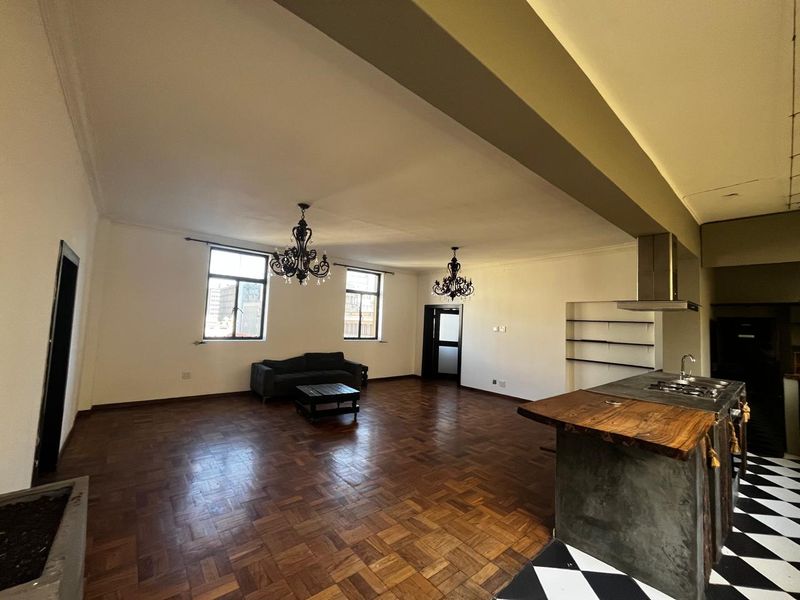 Spacious open-plan living area featuring parquet flooring, a central kitchen island with gas cooktop, and integrated shelving, offering a versatile layout.