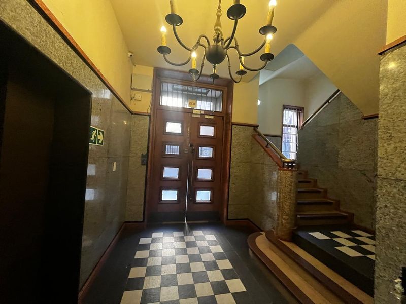 A grand apartment building entrance foyer featuring classic checkered flooring, stone wall finishes, a decorative chandelier, and a staircase.