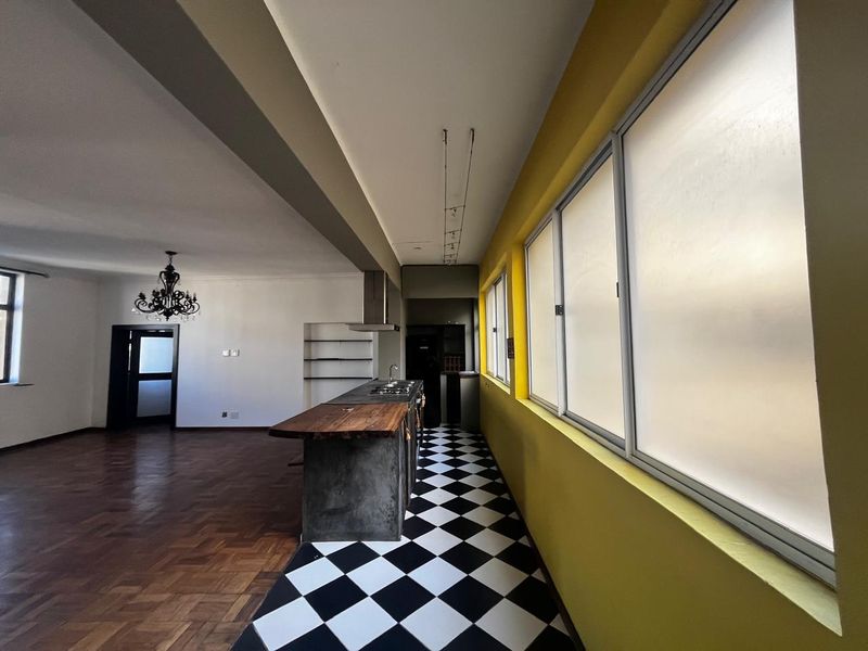 Spacious open-plan living and kitchen area featuring a central island, parquet flooring, and a distinctive checkered tile kitchen floor with built-in shelving.