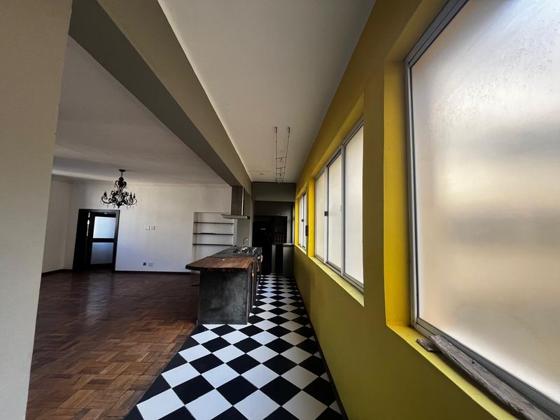 Spacious open-plan living and kitchen area featuring a central island, parquet flooring, and distinctive checkered tiling, offering a versatile layout for modern living.