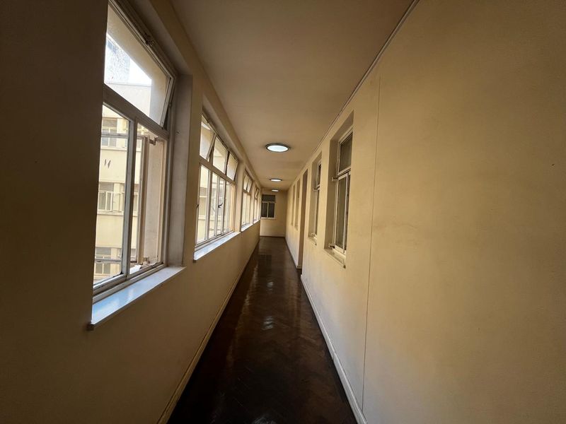 A long, sunlit apartment hallway featuring classic parquet flooring and a series of casement windows along one side.