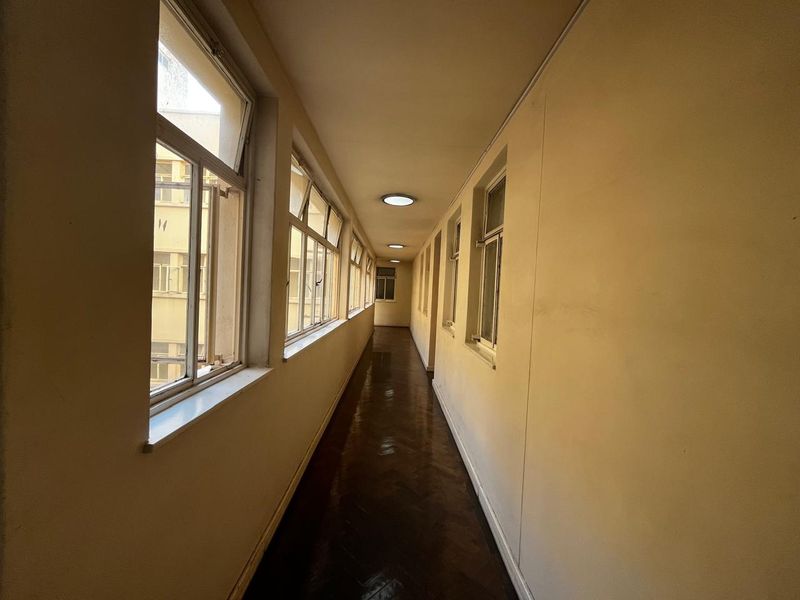 A long, narrow apartment hallway featuring dark parquet flooring, multiple casement windows, and flush-mounted ceiling lighting.