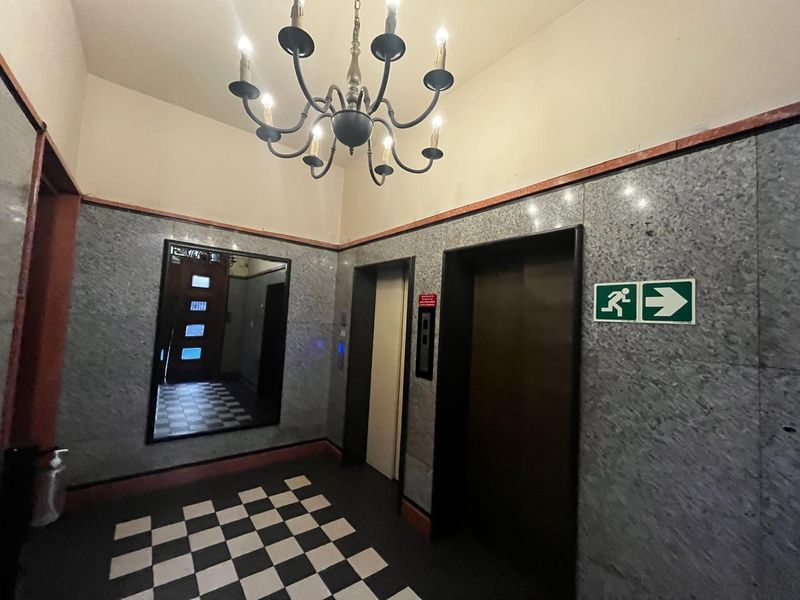 A well-maintained apartment building lobby featuring marble wall cladding, a classic chandelier, and a distinctive checkered floor pattern with elevator access.