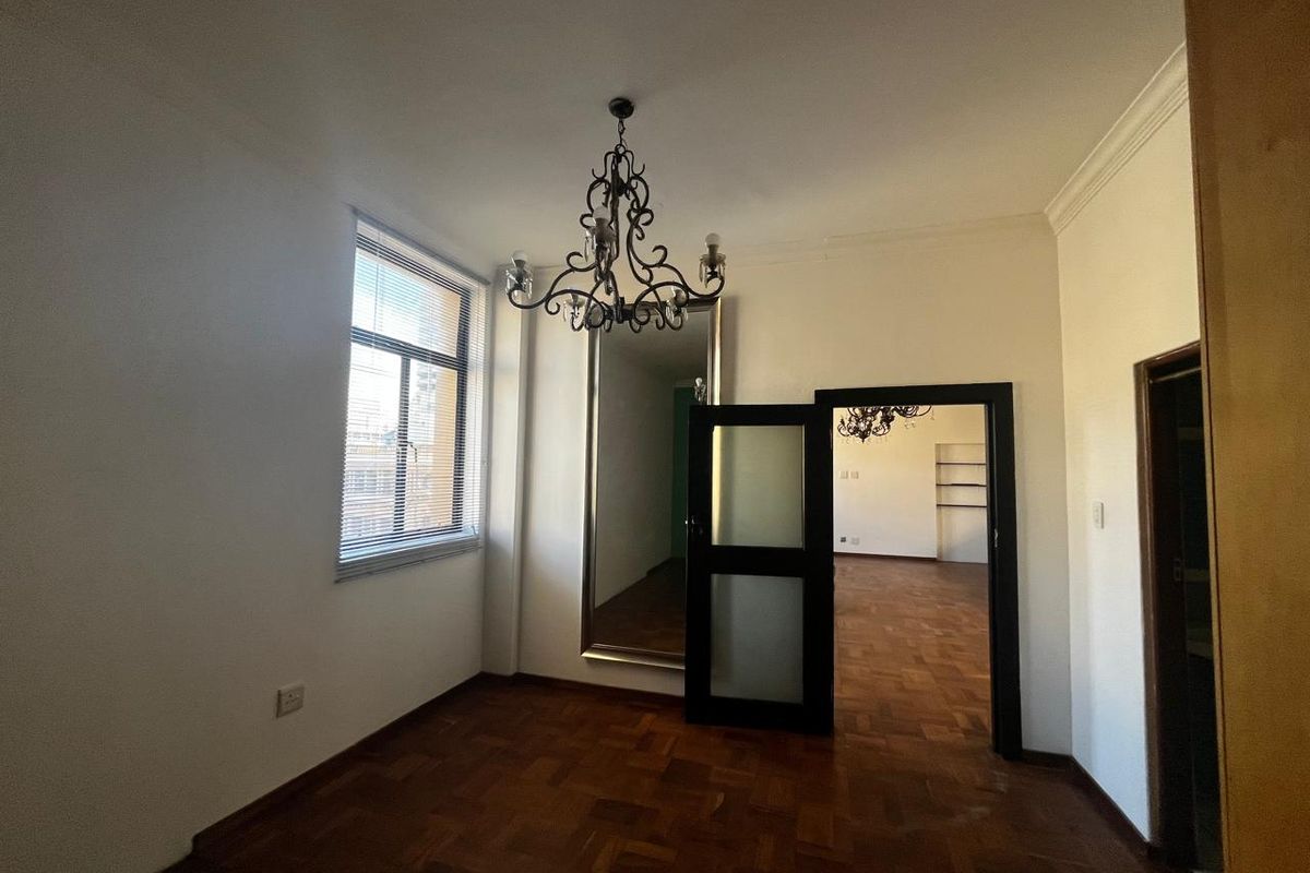 An empty living area featuring classic parquet flooring, an ornate chandelier, and a frosted glass door leading to an adjacent room.