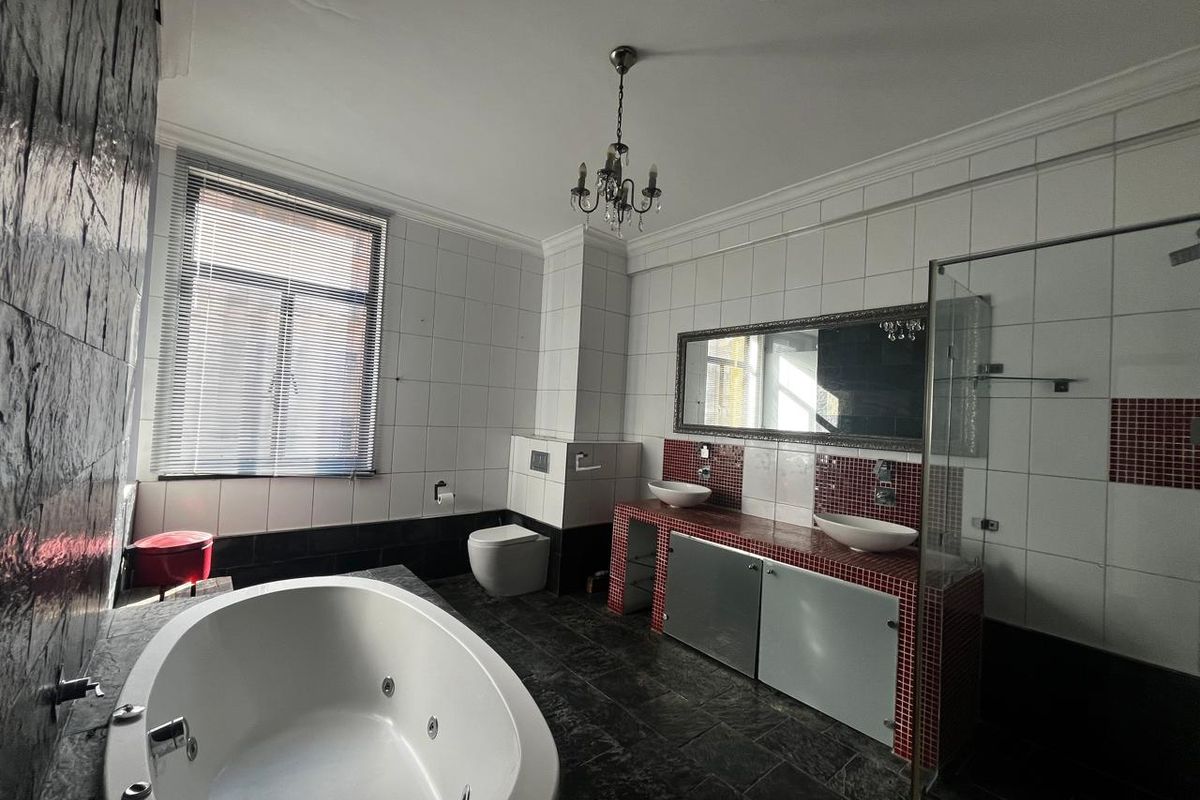 Spacious bathroom featuring a built-in jetted bathtub, dual vessel sinks on a tiled vanity, wall-mounted toilet, and a separate glass-enclosed shower area.