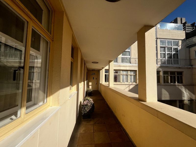 A covered outdoor walkway or balcony featuring tiled flooring and concrete structural pillars, providing access to apartment units.