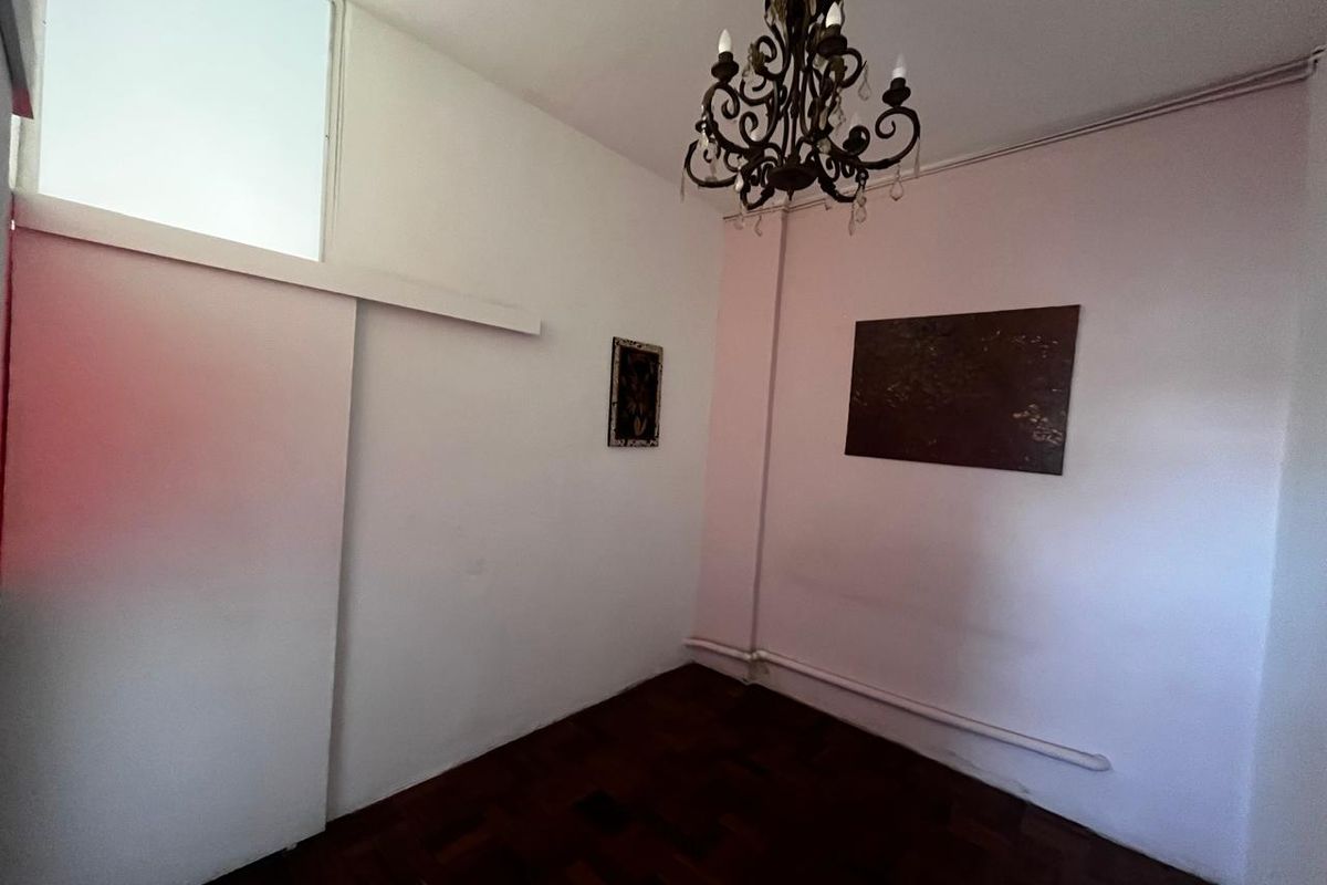 An empty bedroom featuring dark parquet flooring, a transom window, and a sliding door, with visible wall wear and exposed conduit.