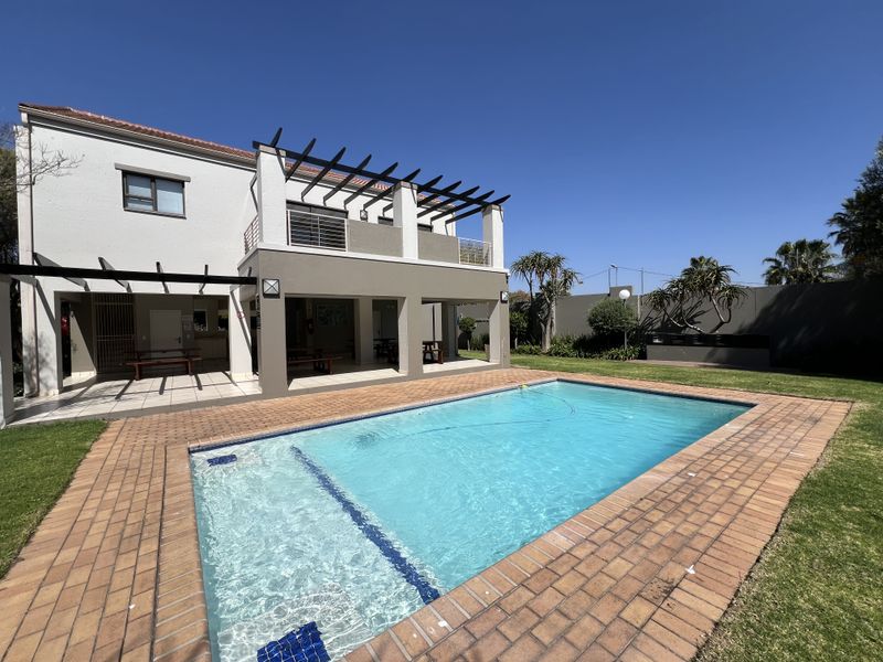 A well-maintained outdoor pool area featuring a swimming pool, paved surround, and a covered patio with a pergola structure.