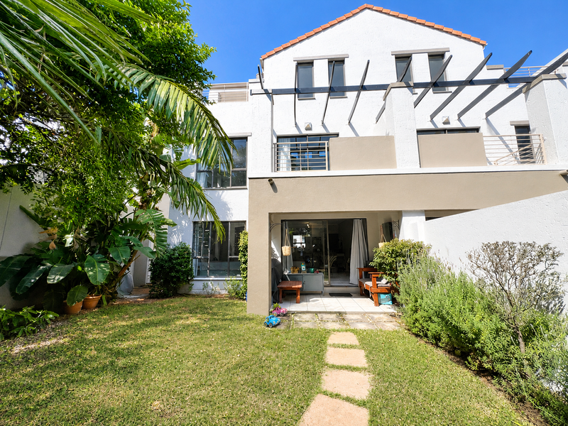 Rear view of the apartment featuring a private garden, tiled patio area with pergola, and upper-level balconies with sliding door access.