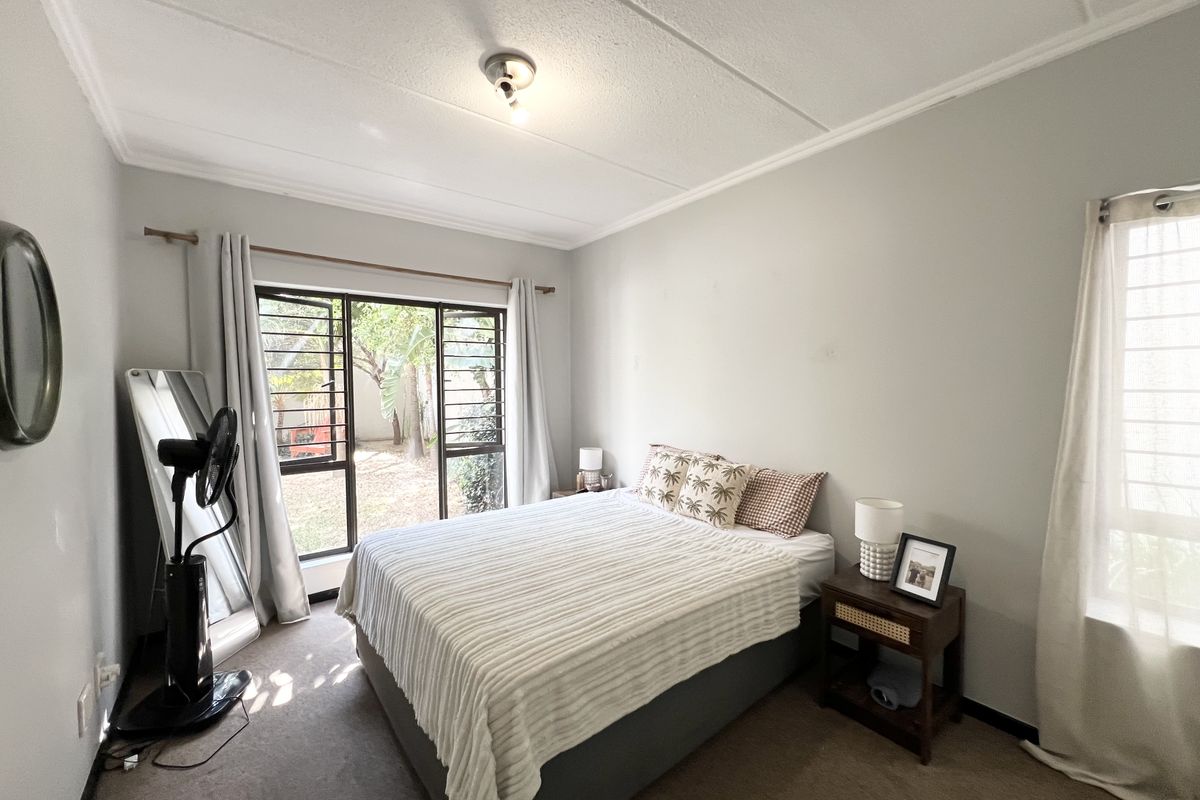 A well-lit bedroom featuring carpeted flooring, a coved ceiling, and a sliding door with security bars providing access to the exterior.