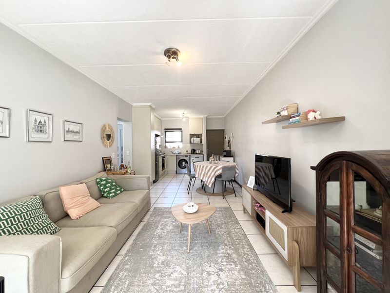 An open-plan living and kitchen area featuring tiled flooring, neutral walls, and a functional kitchen layout with built-in cabinetry and appliances.