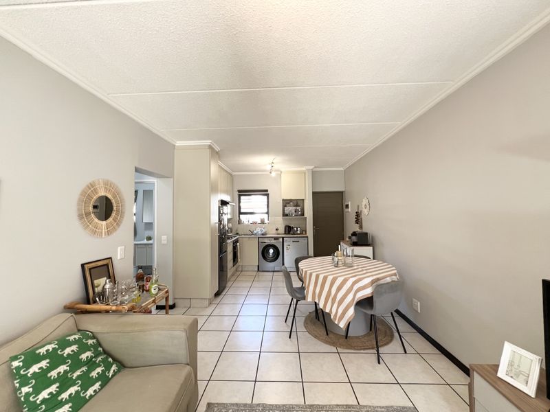 Open-plan living and dining area featuring tiled floors and a functional kitchen with built-in cabinetry, integrated appliances, and laundry plumbing.