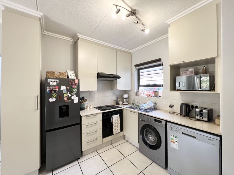 Compact kitchen featuring neutral cabinetry, tiled flooring, integrated oven and hob, and dedicated space for laundry and dishwashing appliances.