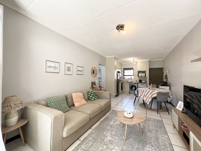 Open-plan living and dining area featuring tiled flooring and a functional kitchen with built-in cabinetry and integrated appliances.