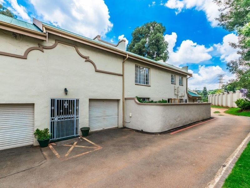 Front exterior view of the townhouse featuring two garage doors, a secure pedestrian entrance, and an asphalt driveway with boundary walling.