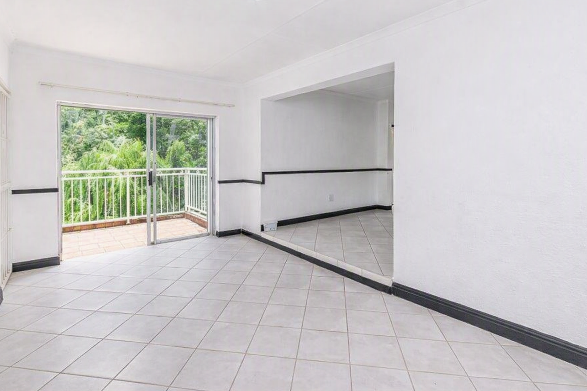 An empty, open-plan living area featuring neutral tiled flooring, a sliding glass door leading to a balcony, and classic coving details.
