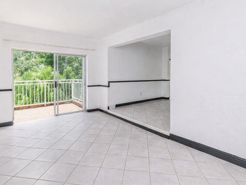 An empty, open-plan living area featuring neutral tiled flooring, a sliding glass door leading to a balcony, and classic coving details.