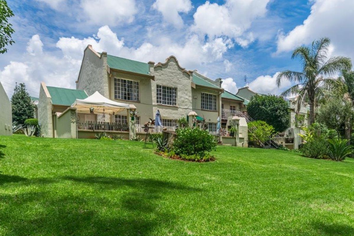 Rear view of a townhouse complex featuring a well-maintained lawn, paved patio areas, and traditional architectural styling with pitched metal roofing.