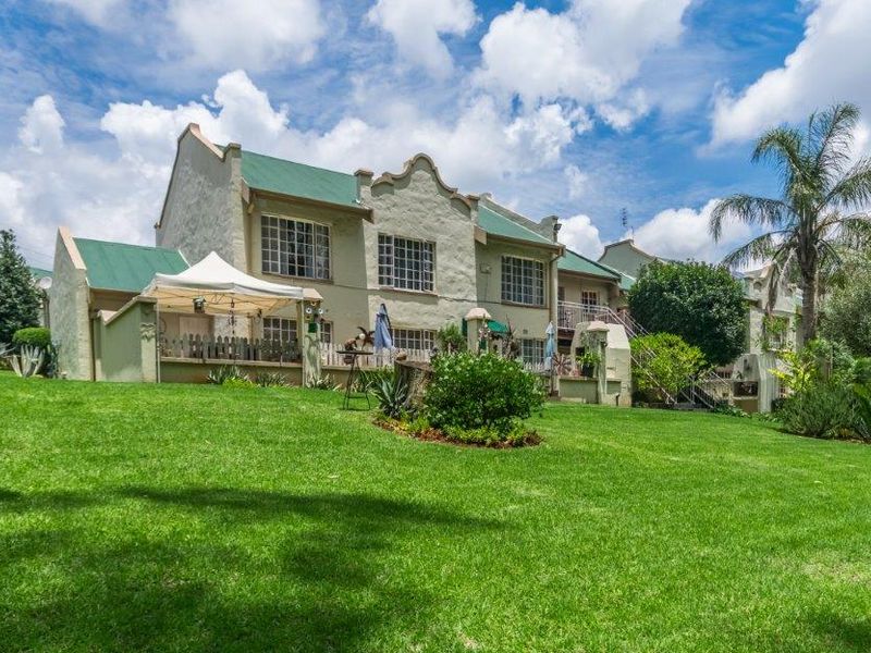 Rear view of a townhouse complex featuring a well-maintained lawn, paved patio areas, and traditional architectural styling with pitched metal roofing.