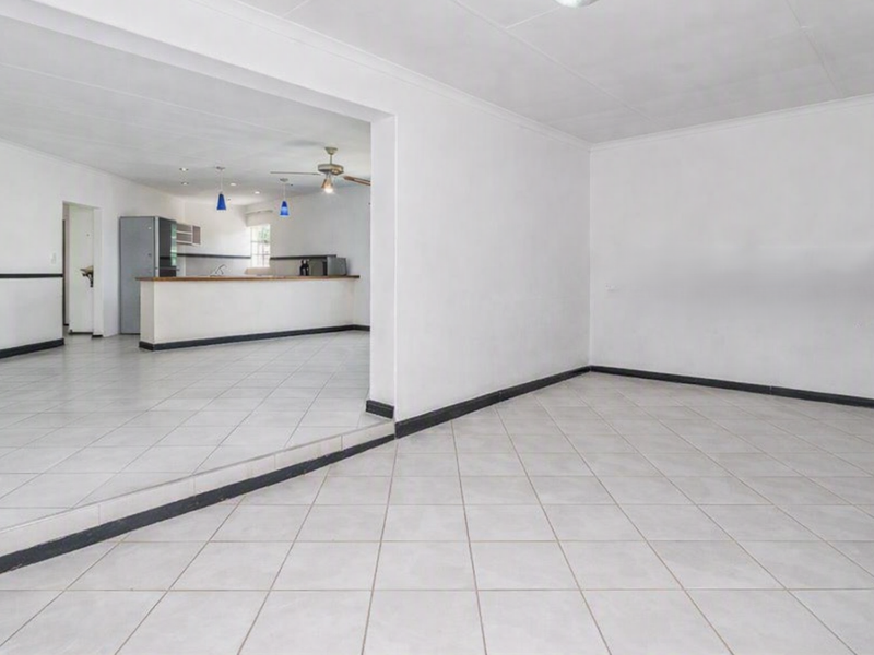Spacious open-plan living and kitchen area featuring neutral tiled flooring, a breakfast bar, and a clean, blank canvas layout.