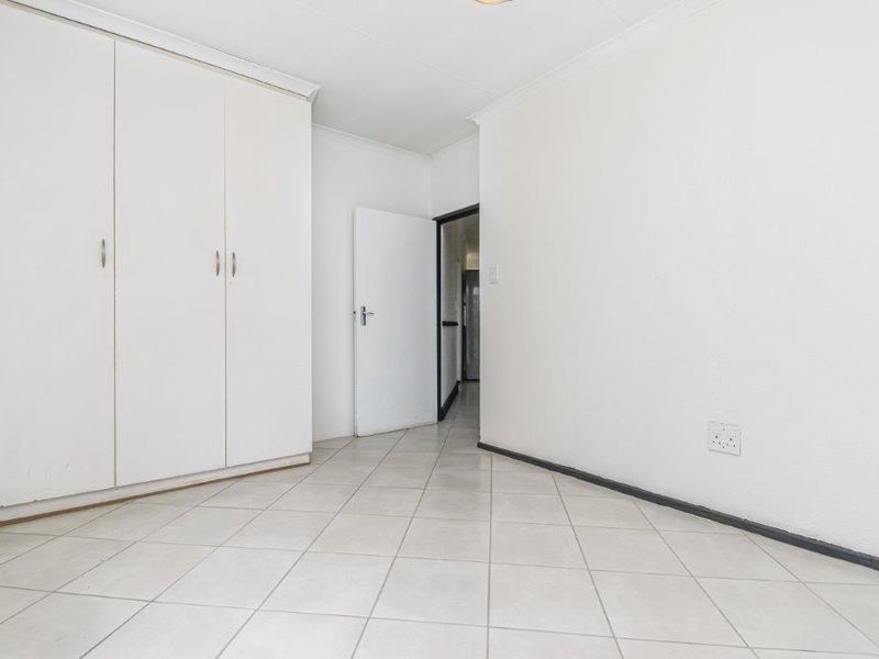 A bright, empty bedroom featuring neutral tiled flooring, built-in cupboards, and coved ceilings, offering a clean canvas for personalization.