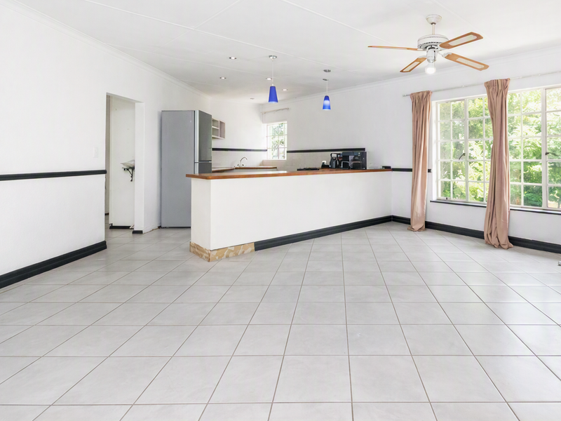 Spacious open-plan living and kitchen area featuring neutral tiled flooring, a breakfast bar, and large windows providing ample natural light.