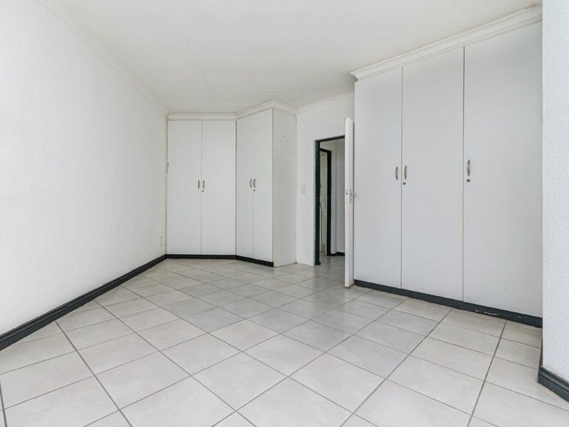 An empty bedroom featuring neutral tiled flooring and extensive built-in cupboard storage, providing a clean and functional space ready for personalization.