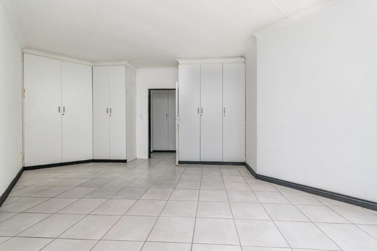 An empty bedroom featuring neutral tiled flooring and extensive built-in cupboard storage, offering a blank canvas for personalization.