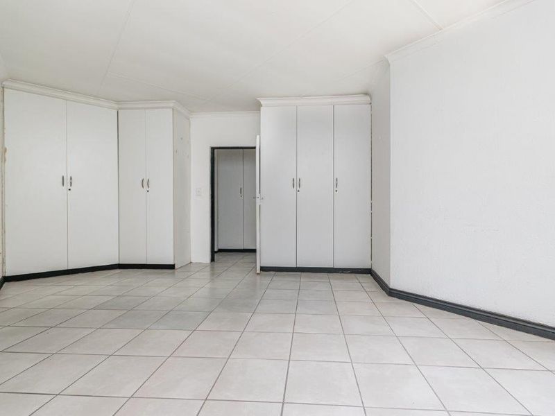 An empty bedroom featuring neutral tiled flooring and extensive built-in cupboard storage, offering a blank canvas for personalization.