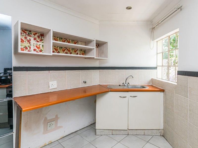 A compact kitchen area featuring laminate countertops, a stainless steel sink, tiled backsplash, and basic built-in cabinetry, requiring some cosmetic updates.