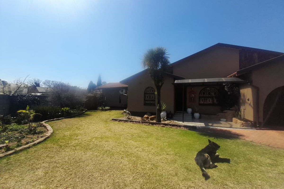 A view of the rear exterior of the house featuring a covered patio, paved areas, and a well-maintained garden.