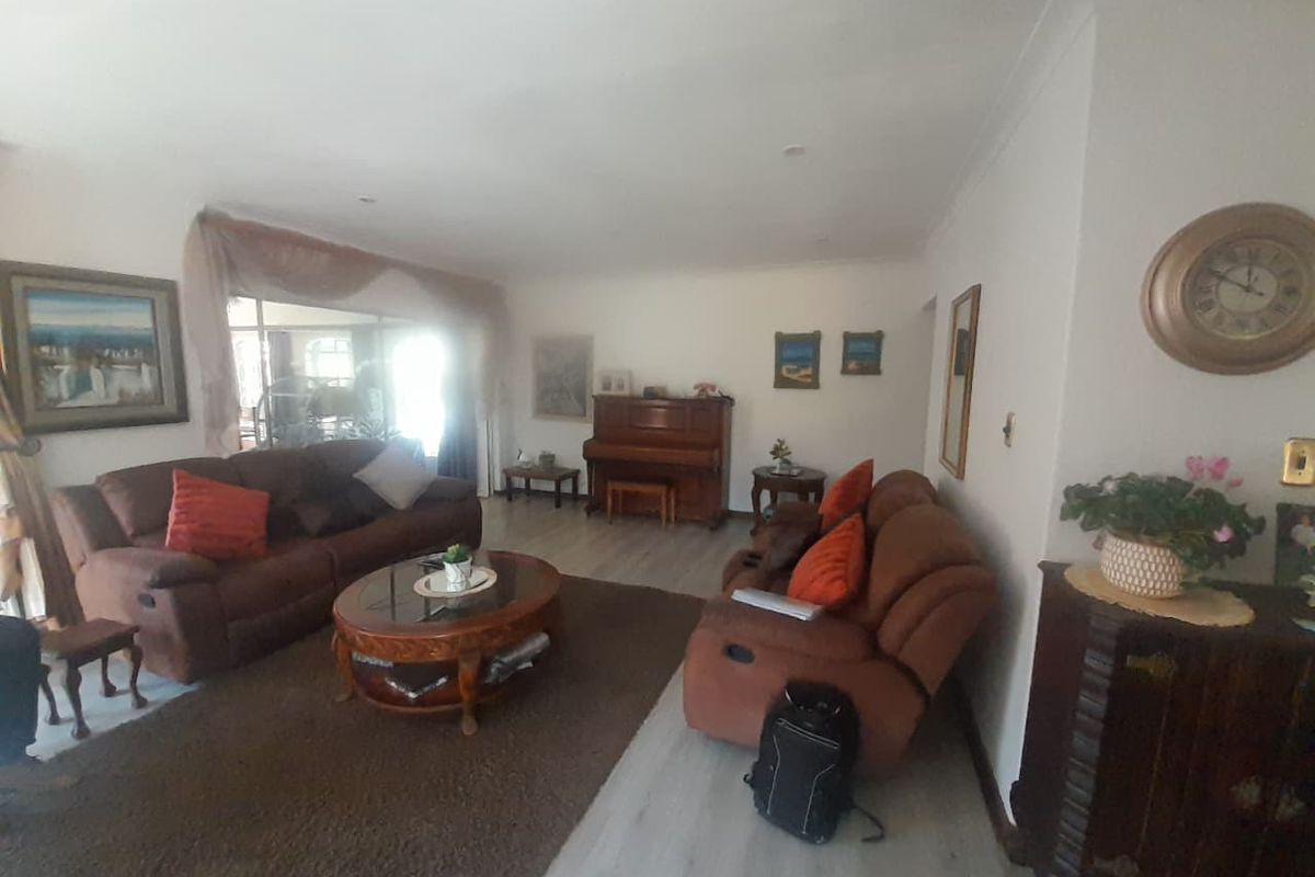 A spacious living room featuring light-toned laminate flooring and cove cornicing, offering a neutral base for interior updates.