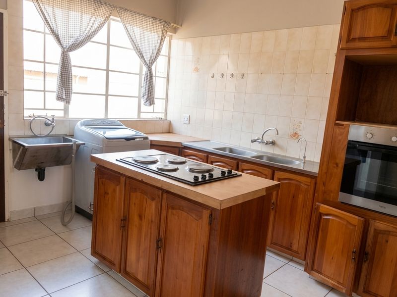 Functional kitchen featuring wooden cabinetry, built-in oven, electric hob, double sink, and a separate utility sink area with tiled finishes.