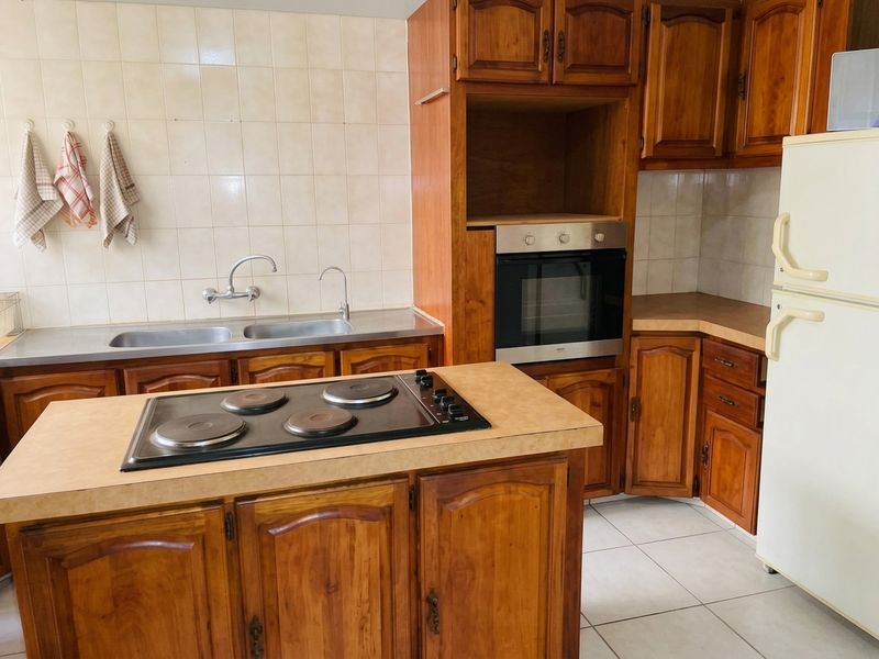 A functional kitchen featuring traditional wooden cabinetry, a built-in oven, electric hob, and a double basin stainless steel sink with tiled backsplash.