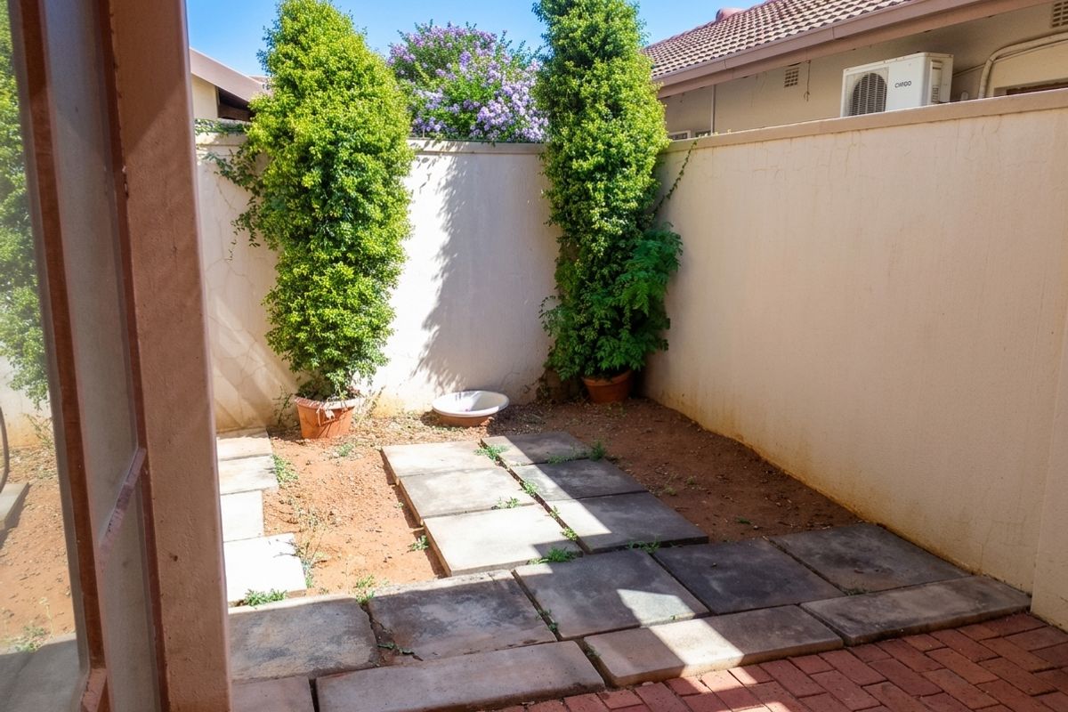 A compact rear courtyard area featuring a boundary wall, paved sections, and established greenery, offering potential for a private outdoor retreat.