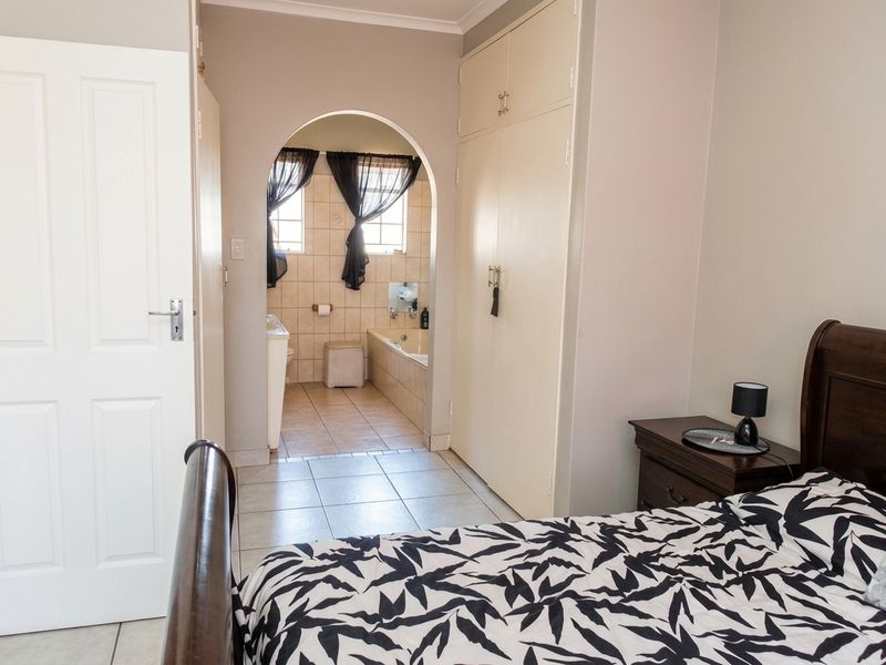 A bedroom featuring built-in cupboards and an arched entryway leading to an en-suite bathroom with tiled flooring.