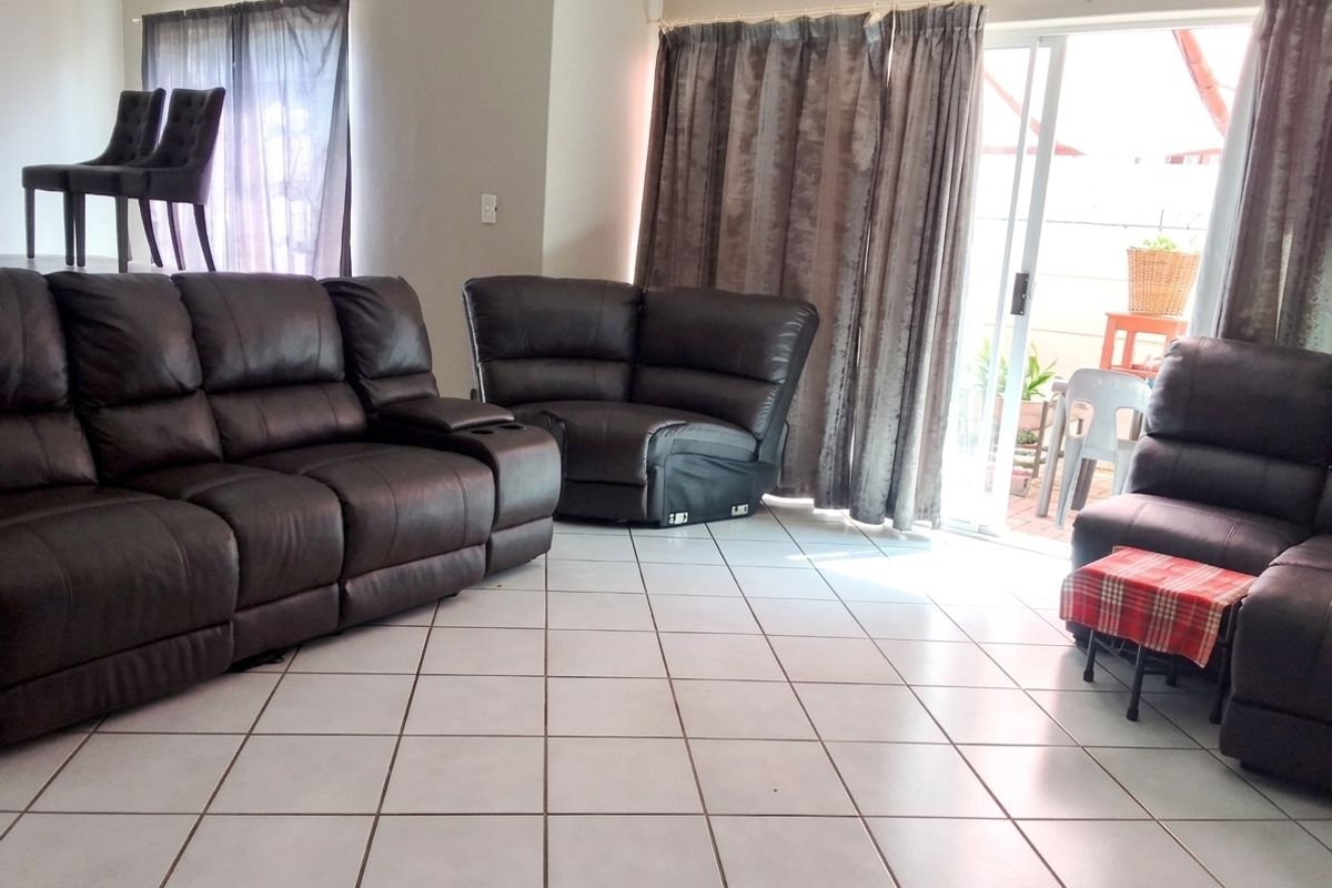 Spacious living room featuring neutral ceramic floor tiles and a large sliding glass door providing access to the outdoor patio area.
