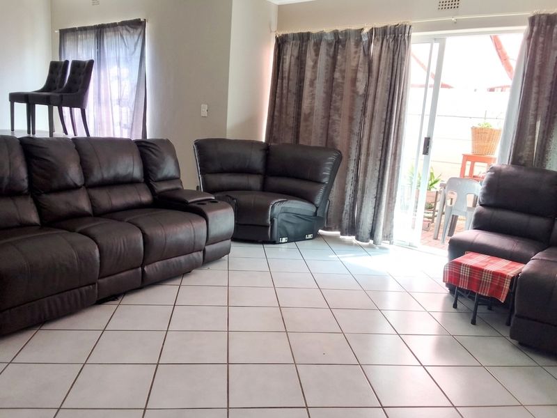 Spacious living room featuring neutral ceramic floor tiles and a large sliding glass door providing access to the outdoor patio area.