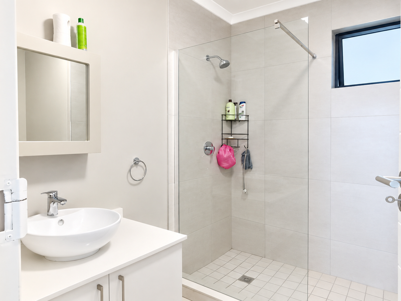A clean, modern bathroom featuring a vessel sink vanity, a spacious walk-in shower with a glass screen, and neutral wall tiling.