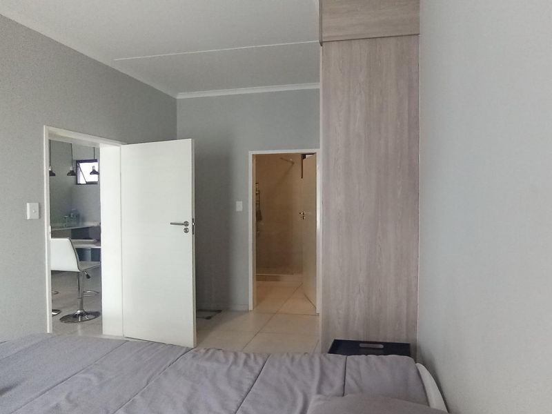 A bedroom featuring neutral grey walls, tiled flooring, and a built-in wardrobe, with direct access to an en-suite bathroom and adjacent living area.
